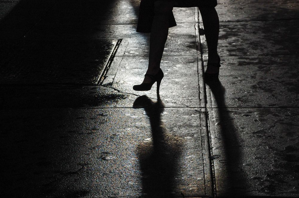 A woman’s foot wearing a high heel shoe casting a stark shadow on the pavement 