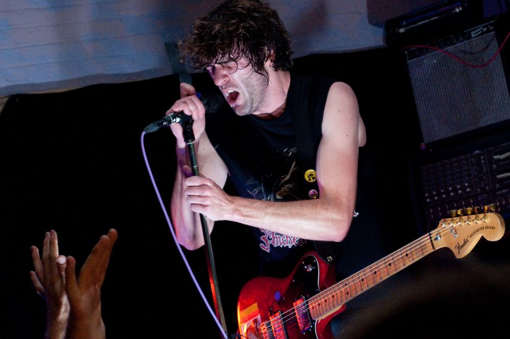 Brian King from the band Japandroids singning into a microphone with his eyes closed. 