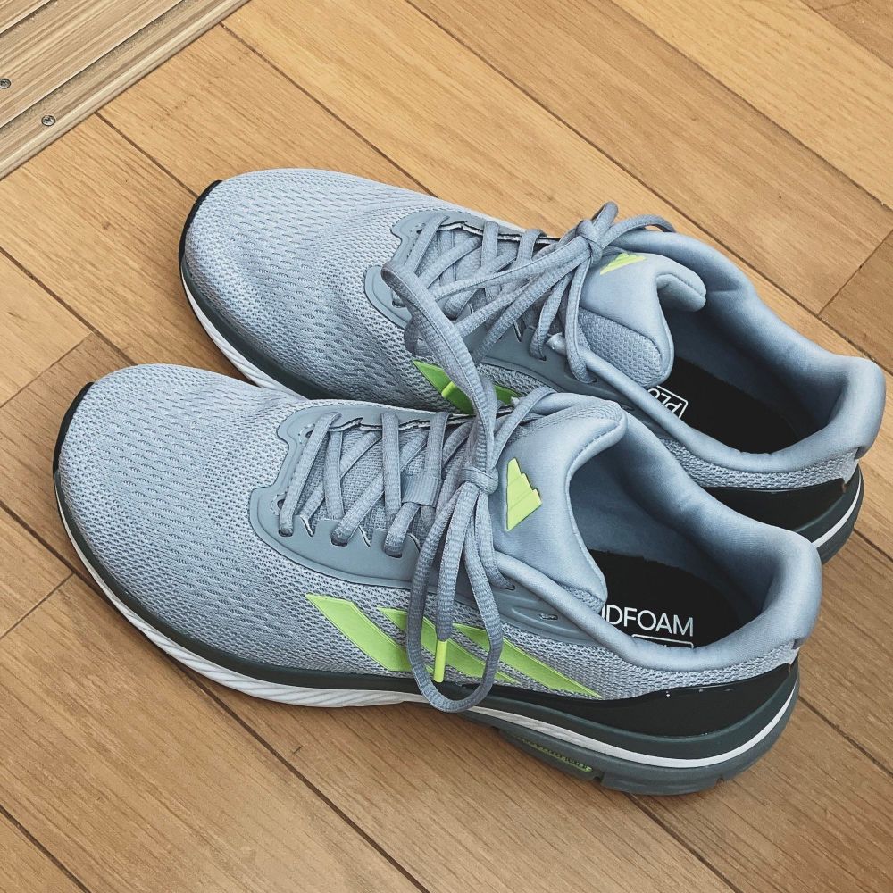 フローリングに置かれたスニーカーの写真。
少しスポーティな流線的デザイン、明るいグレーに蛍光グリーンの差し色。