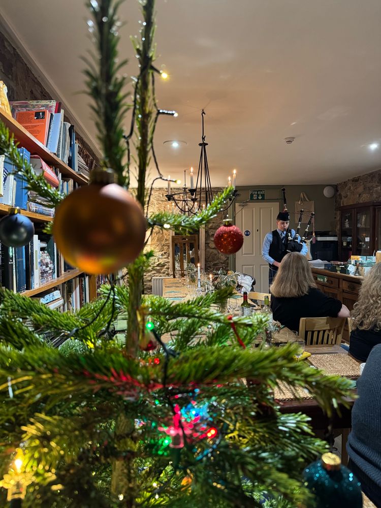 A piper playing bagpipes beyond a Christmas tree