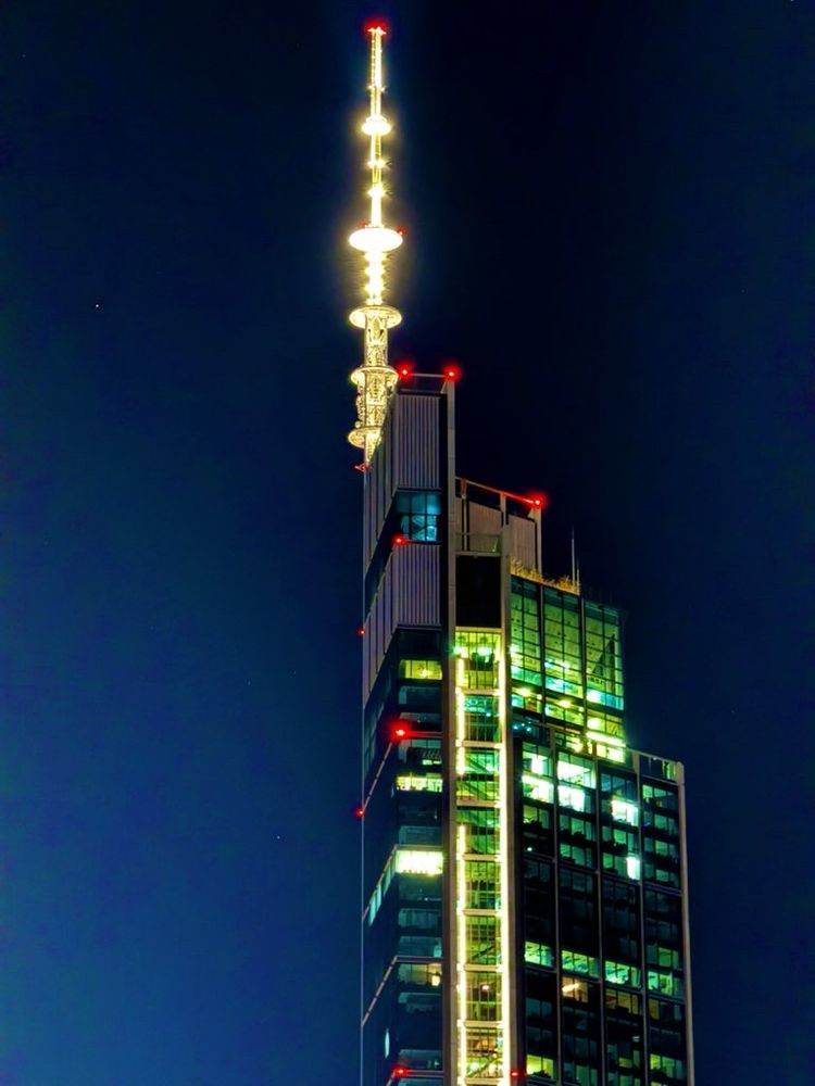 A skyscraper office block with a radio antenna on top in Warsaw. It is glowing against the night sky.