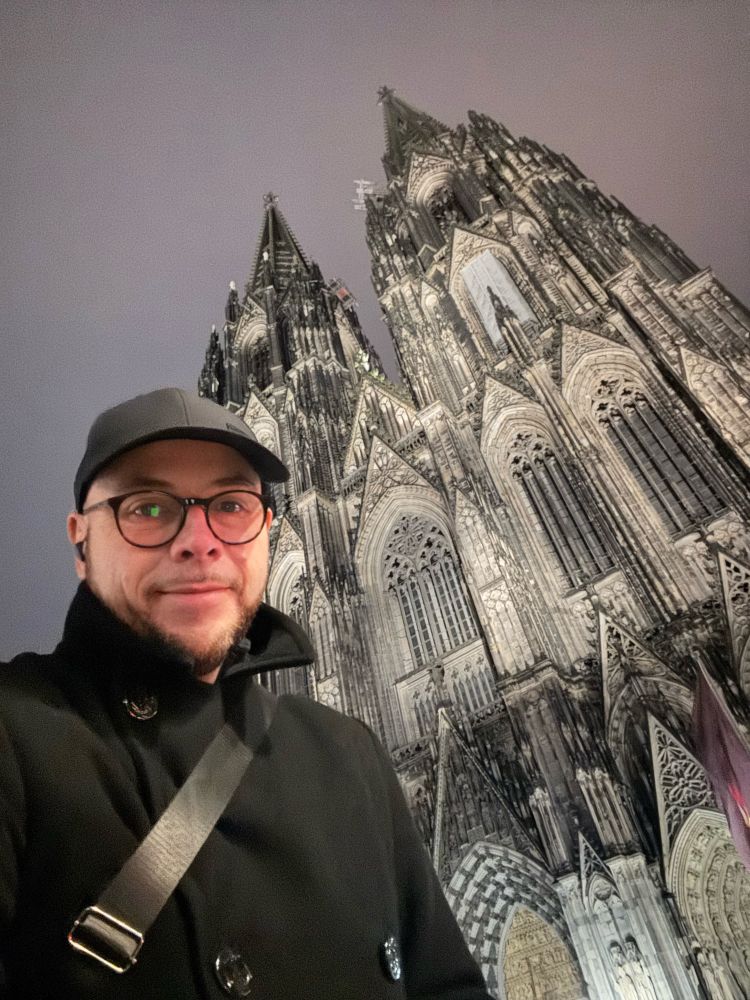 Kris, a man with round glasses and a black baseball cap, outside Cologne Cathedral.