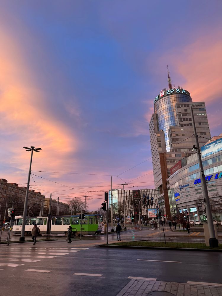 A colourful sky above a modern skyscraper in Szczecin Poland. A green and white tram is passing by