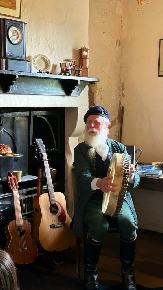Storyteller Tony Bonning singing and playing a drum in the historic kitchen at Ellisland. He is in traditional folk dress.