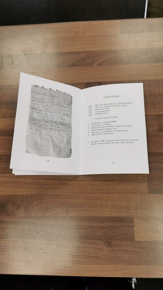 a small booklet laying open on a wooden table, with a handwritten recipe on notepaper on the left for highland shorties, and on the right, a vegan version