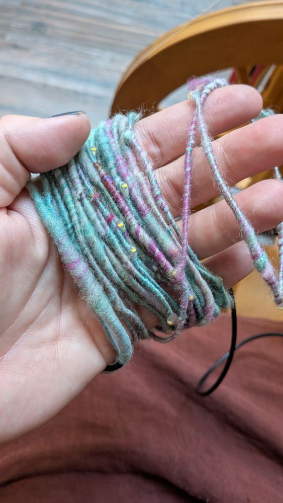 A hand wrapped in fairy light yarn.  The lights are turned off to show the colors of the yarn, which is streaked with minty green and pink wool and silk.