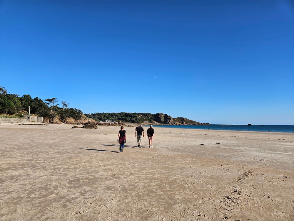 Three figures on a sandy beach with sea and rocky headland in the distance 