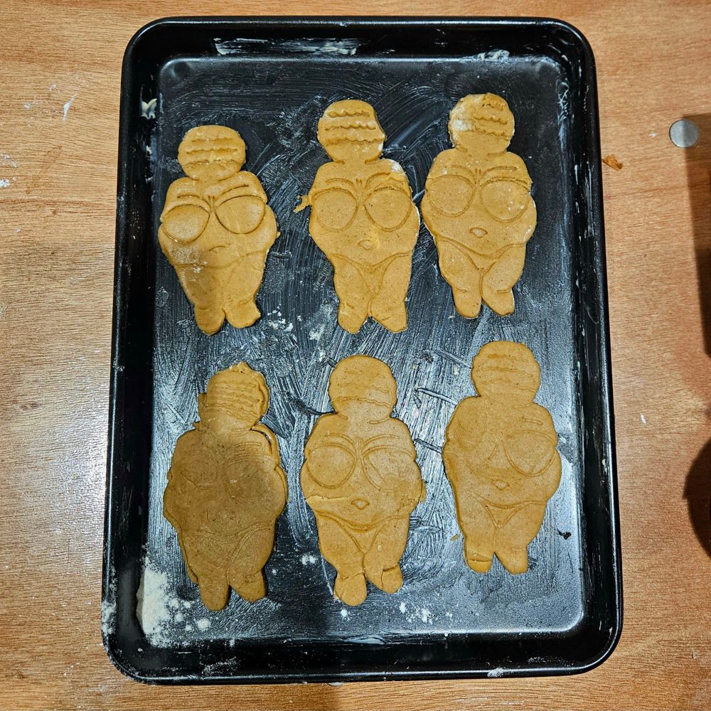 Six Cookies in the shape of the Venus of Willendotf lined up.on a baking tray 