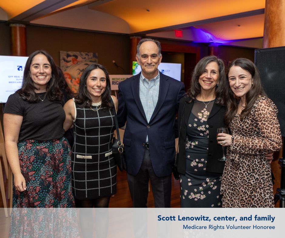 An audience that is mostly seated, facing a stage on the right, with some audience members standing further behind. 