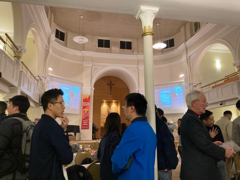 Various people inside a church building with red banners with Chinese and English on the wall 
