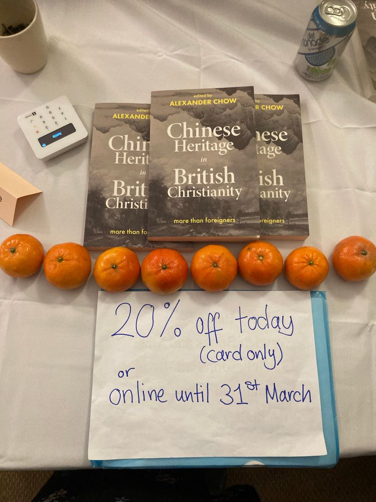 A row of eight mandarins with 3 copies of the book ‘Chinese Heritage in British Christianity’ and a card payment machine on top of a white tablecloth 
There is a sign telling you that there is 20% off the book today (card only) or online until 31st March