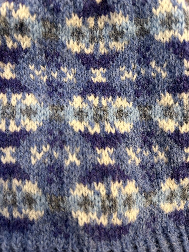 A picture of Shetland style knitting in shades of blue and grey, showing a repeating pattern of globe shapes like Xmas baubles. 