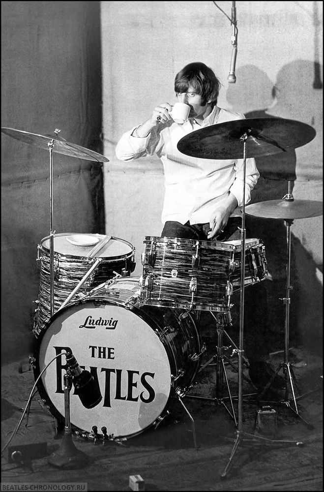 Ringo Starr drinking a cup of tea while sitting at his drum kit in Abbey Road Studio 2. The saucer is balanced on one of his drums.