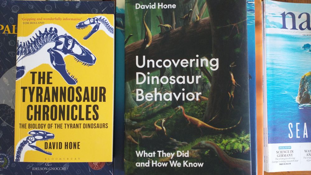 "The tyrannosaur chronicles" and "Uncovering dinosaur behavior", both by Dr. David Hone, on a couple of piles of science books and journals.