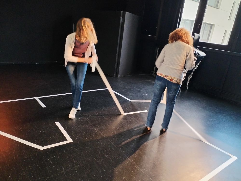 Deux personnes en train de décoller du ruban adhésif blanc qui a servi a délimité les contours d'une scène de théâtre. 