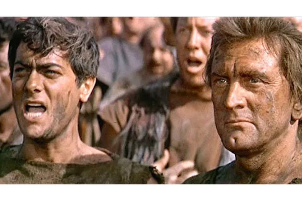 A still from the 1960 Stanley Kubrick film Spartacus, featuring Tony Curtis and Kirk Douglas, of Curtis as Antoninus saying, “No, I am Spartacus.”
