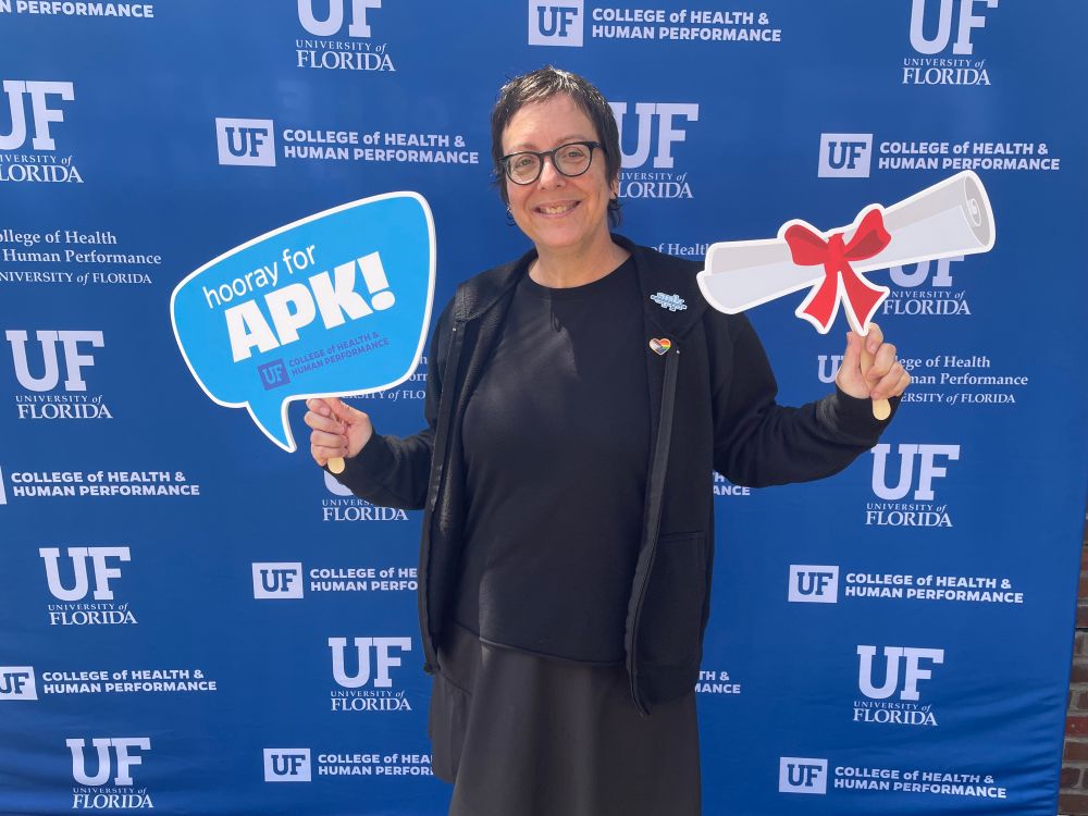 Aging hipster holding goofy signs in front of University Of Florida backdrop. 