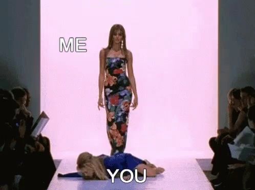 a woman in a floral dress is walking down a runway next to a woman laying on the floor .