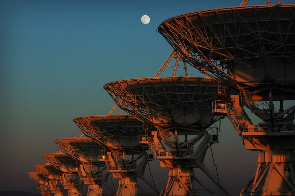 The moon rises over the NRAO Very Large Array radio telescope in New Mexico during sunset.