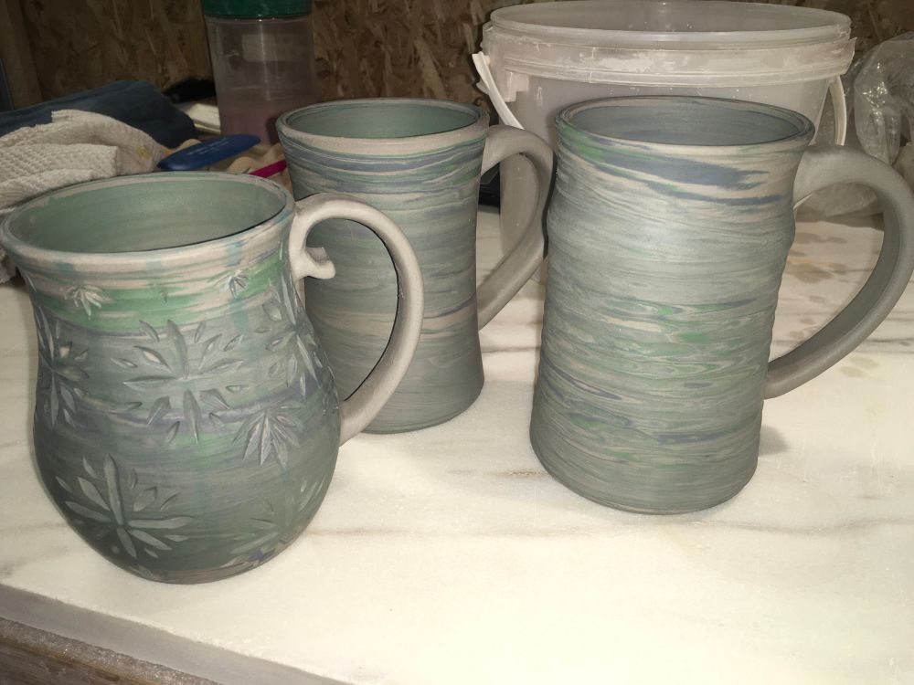 Three mugs of different shapes, thrown with white, green and black coloured clays to create a marbling effect.  All pictured before first firing.