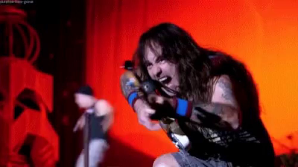 a man with long hair is singing into a microphone in a dark room