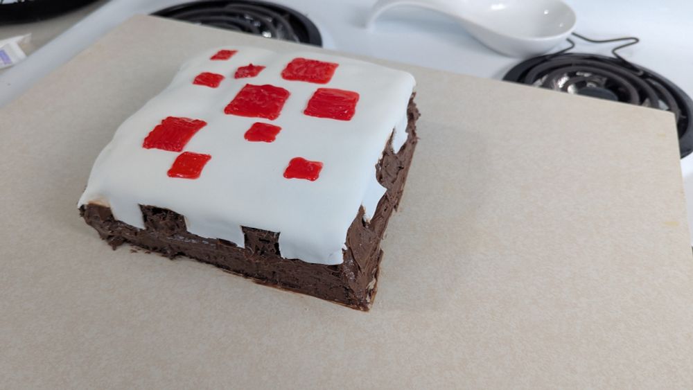 A chocolate cake with white fondant and red gel icing. It's in the style of the cakes found in the game of Minecraft