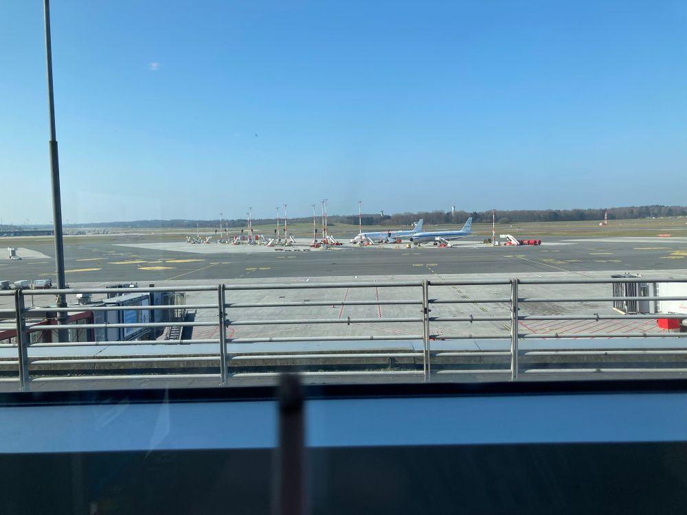 Im Vordergrund eine Zigarette. Dahinter das Rollfeld des Flughafens. 