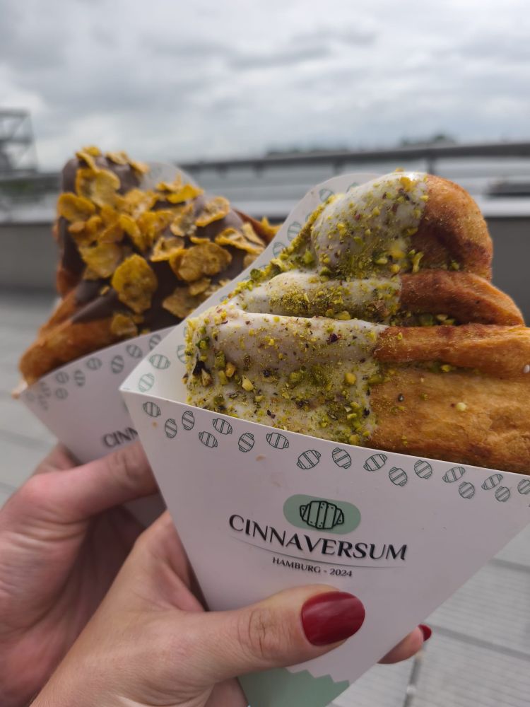 Zwei Franzbrötchen. Eines mit Pistazien und eines mit Cornflakes. Im Hintergrund der Hamburger Hafen. 