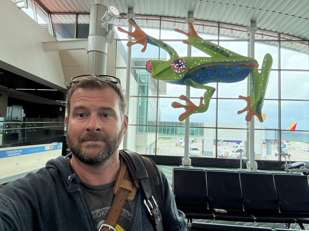 Selfie of man in front of a large Red-Eyed Treefrog sculpture in an airport