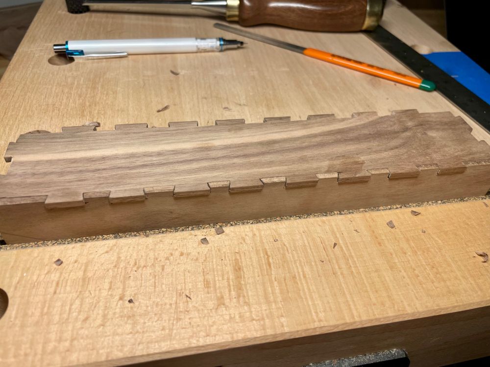 Photo of two very thin pieces of dark wood with a fresh dovetail joint with 8 tails and 9 pins. 