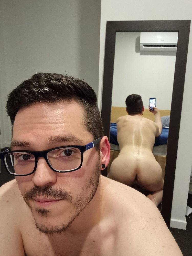 Me kneeling on the floor at the foot of my bed with my back and ass visible in a mirror 