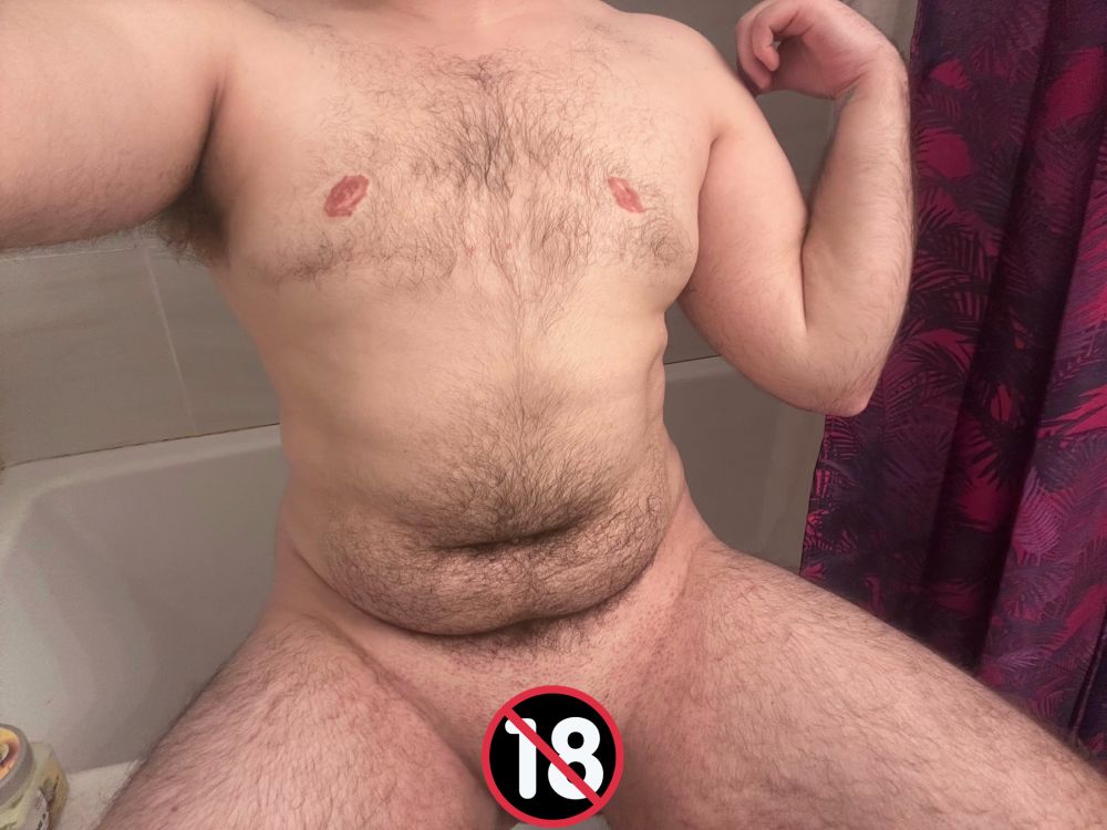 TransGuyKink is pictured, from his knees to below his neck, sitting on the edge of a tub. 
You can see his fluffy armpit hair, stomach hair, leg hair, and chest hair. It all looks so soft and inviting.
He's lightly flexing his left arm and proudly showing off his top surgery scars.
He looks like the perfect man to curl up with in a nice hot bath.