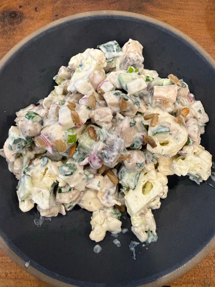 a bowl of chopped salad with cauliflower, mushrooms, radish, green onions, chickpeas, and sunflower seeds all in a yogurt dressing 
