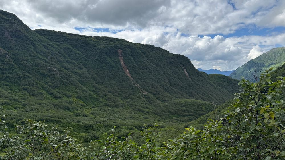 A green valley with a small landslide, blue sky and some clouds. 