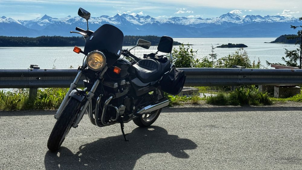 A motorcycle parked on the side of the road with the ocean and mountains in the background. 