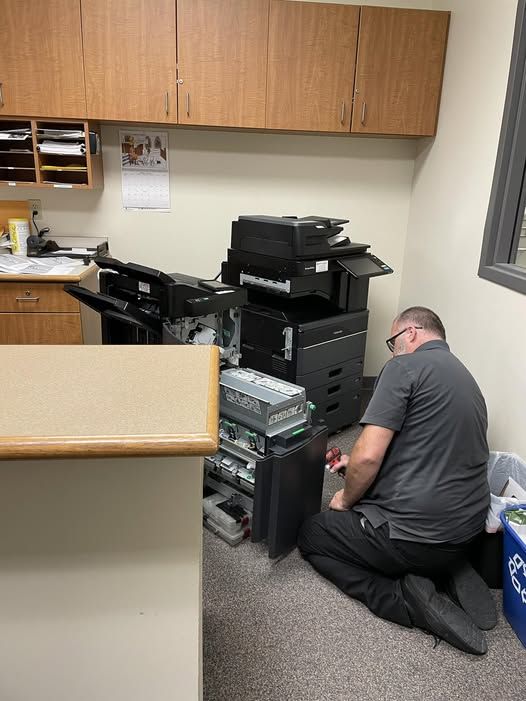copier technician with many parts of a copier pulled apart