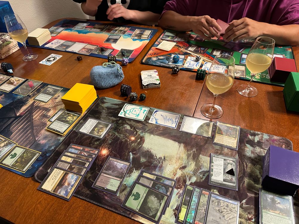 An overview of a table where a commander game is being played. There a wine glasses spread out on the table. 
