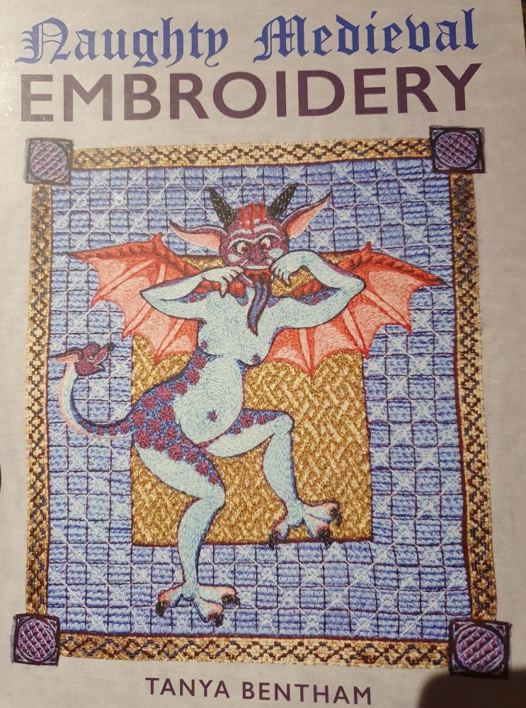 Cover of a book called Naughty Medieval Embroidery, by Tanya Bentham. The centre of the cover shows a blue medieval demon, with red pink bat wings, and red scales on its butt. Its tail has a dog or fox head on the tip. The demon's face is purple and it's sticking out it's tongue. It's ears are big, pointy and go sideways from the head, making room for black horns to point out the top. The background is a gold patterned square, in a bigger blue chequered square, and a gold border.