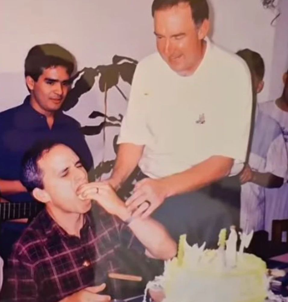Padre Prevost comendo um bolo com a mão tal como um selvagem, observado por dois homens com expressão de “ow pega leve ae”. Um deles inclusive está com a mão no braço dele