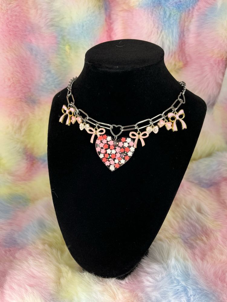 A charm necklace featuring pink bows and a pink cherry blossom resin heart centerpiece 