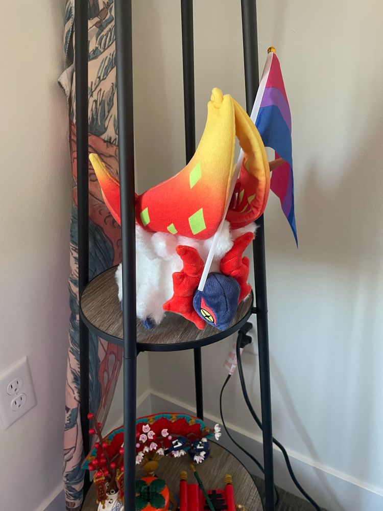A Slither Wing Pokemon plush with a bisexual pride flag supported in its wings. 