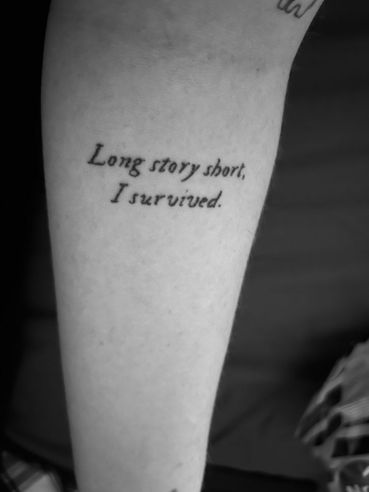 A black and white photo of an arm tattoo saying “long story short, I survived” in a cursive style font 