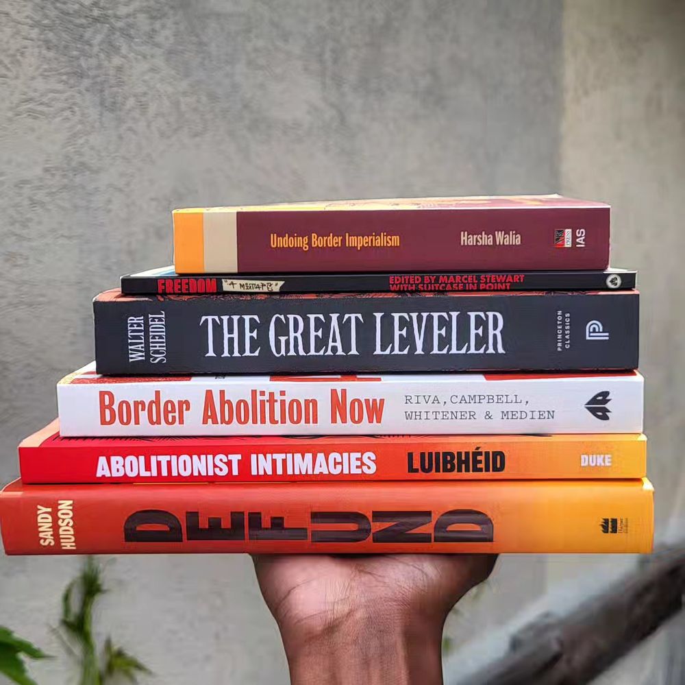 Picture of a hand holding a stack of books:
- Undoing Border Imperialism edited by Harsha Walia
- Freedom, A Mixtape edited by Marcel Stewart with Suitcase In Point
- The Great Leveler by Walter Scheidel
- Border Abolition Now by River, Campbell, Whitener, and Medien
- Abolitionist Intimacies: Queer And Trans Migrants Against The Deportation State edited by Luibheid
- Defund: Black Lives, Policing, And Safety by Sandy Hudson