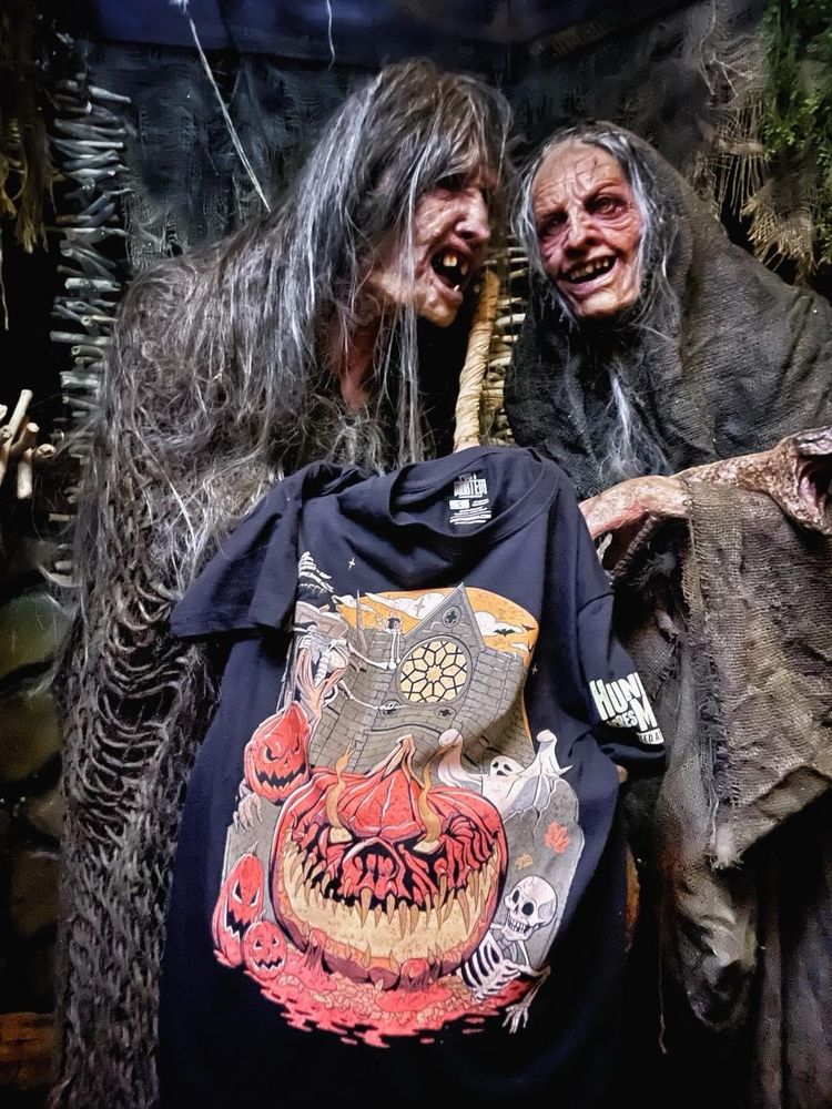 Two wicked witches holding t shirt for Hundred Acres Manor. 