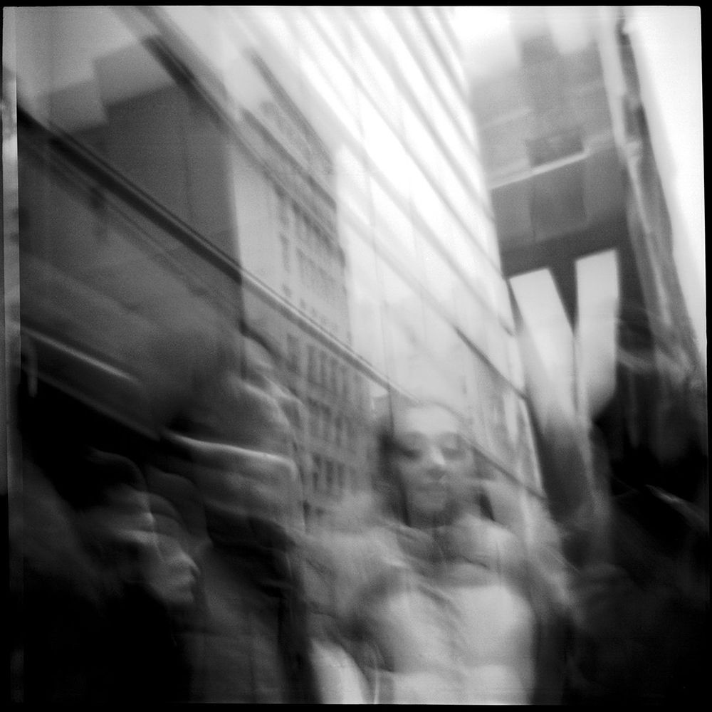 The photograph depicts a street scene in the NOHO part of Manhattan, with blurry figures that appear to be people and tall structures. It is a double exposure created in a tight scene.