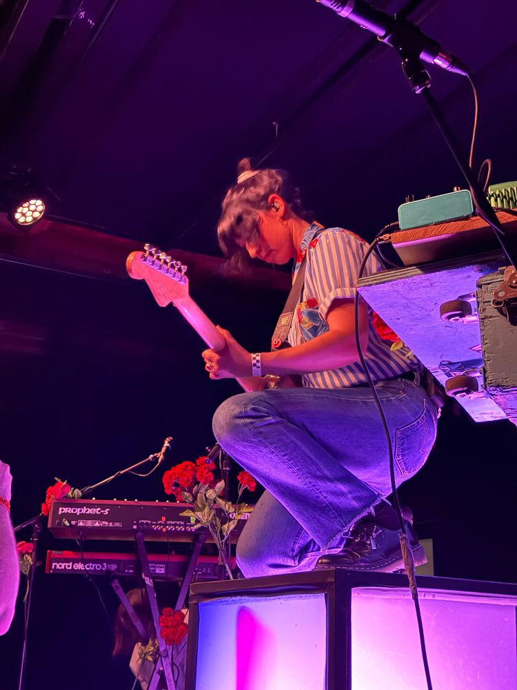 Jessica Dobson playing the guitar on top of a prop on stage while kneeling. 