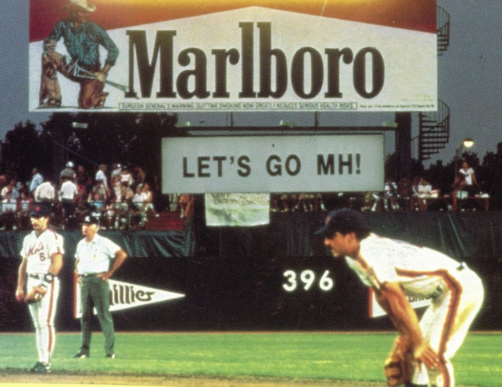 A stadium baseball game is dominated by a huge billboard advertising Marlboro cigarettes.