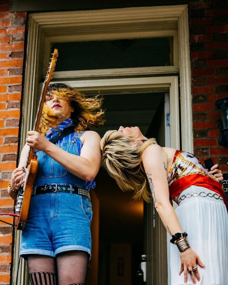 charlie playing guitar and kira holding a microphone & bending over backwards 