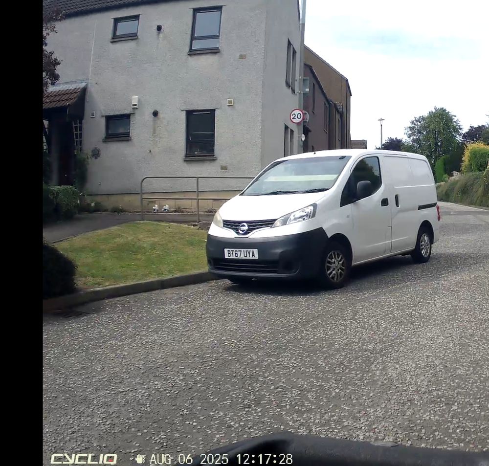 A white van parked in a street, a large long parcel is on the dash obscuring half the windscreen.