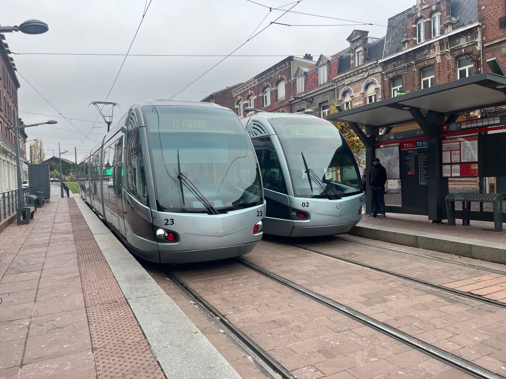 2 Alstom Citadis trams in silver grey livery passing each other at Valenciennes Gare tram stop. 